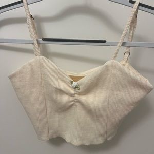 Cream cropped tank top with rosette detail and adjustable straps.